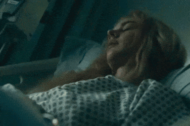 A Woman In A Hospital Gown Is Laying In A Hospital Bed With Her Eyes Closed . GIF