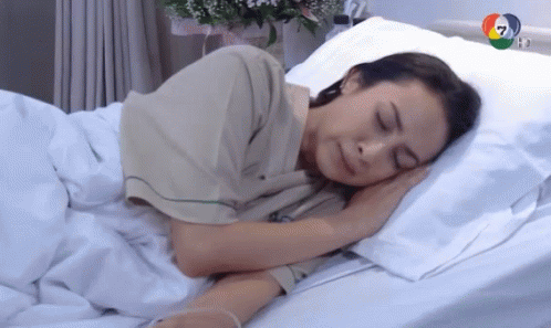 A Woman In A Hospital Gown Is Sleeping In A Hospital Bed GIF