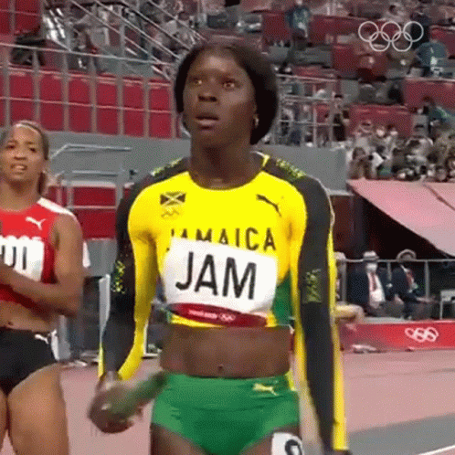 A Woman In A Jamaica Jersey Is Standing On A Track Holding A Stick . GIF