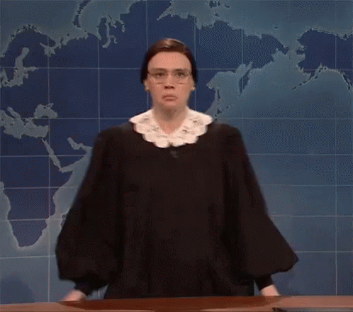 A Woman In A Judge 'S Robe And Glasses Is Standing In Front Of A Map Of The World . GIF