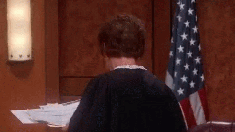 A Woman In A Judge 'S Robe Is Sitting At A Desk In A Courtroom . GIF