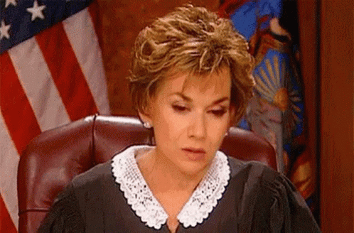 A Woman In A Judge 'S Robe Is Sitting In A Courtroom In Front Of An American Flag . GIF