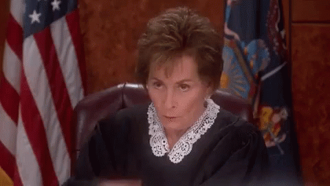 A Woman In A Judge 'S Robe Is Sitting In Front Of An American Flag In A Courtroom . GIF