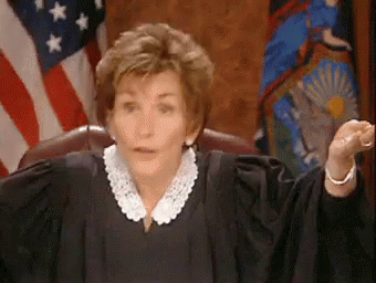 A Woman In A Judge 'S Robe Is Sitting In Front Of An American Flag In A Courtroom . GIF