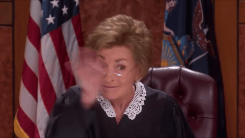 A Woman In A Judge 'S Robe Is Waving Her Hand In Front Of An American Flag GIF