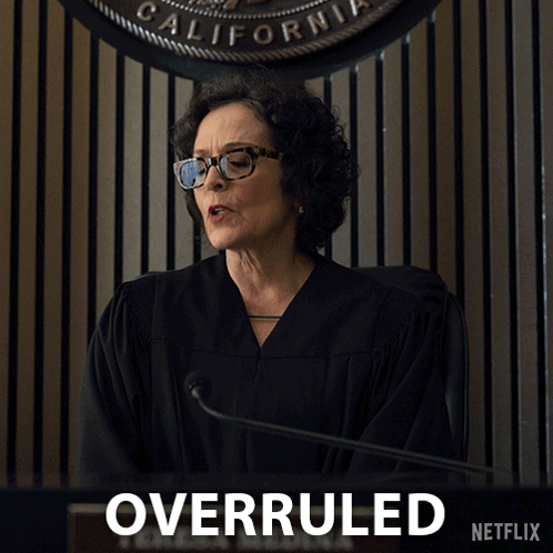 A Woman In A Judge 'S Robe Stands In Front Of A Sign That Says Overruled On It GIF