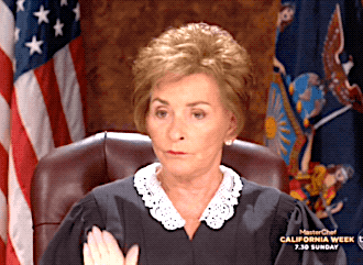 A Woman In A Judge 'S Robes Is Sitting In Front Of An American Flag GIF