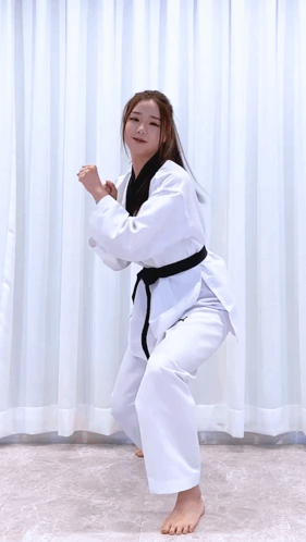 A Woman In A Karate Uniform Is Jumping In The Air While Holding A Sword . GIF