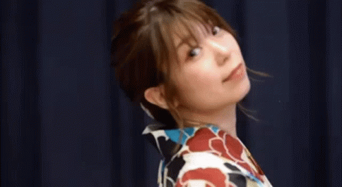a woman in a kimono is standing in front of a blue curtain with her eyes closed .