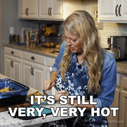 A Woman In A Kitchen With The Words " It 'S Still Very Very Hot " GIF