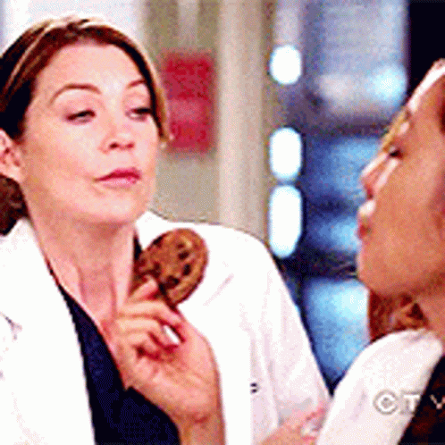 A Woman In A Lab Coat Is Holding A Cookie In Her Hand While Another Woman Looks On . GIF
