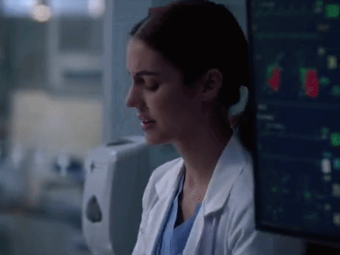A Woman In A Lab Coat Is Sitting In Front Of A Computer Monitor In A Hospital Room . GIF