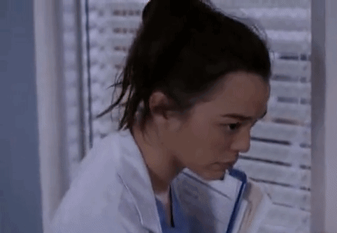 A Woman In A Lab Coat Is Sitting In Front Of A Window Holding A Clipboard . GIF