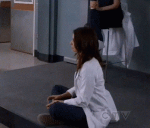 A Woman In A Lab Coat Is Sitting On The Floor In Front Of A Ctv Sign GIF