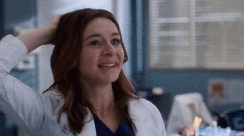 A Woman In A Lab Coat Is Smiling While Holding Her Hair . GIF