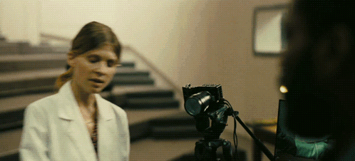 A Woman In A Lab Coat Is Talking To A Camera GIF