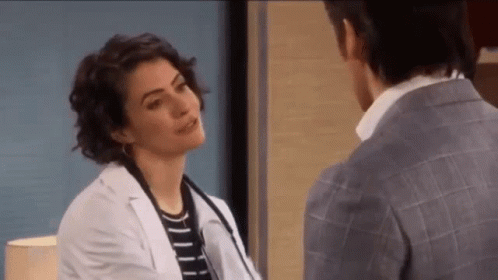 A Woman In A Lab Coat Is Talking To A Man In A Suit In A Hospital Room . GIF