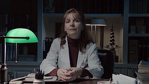 A Woman In A Lab Coat Sits At A Desk GIF