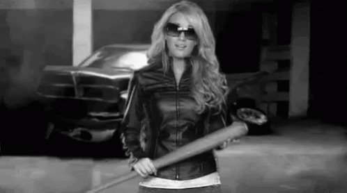 A Woman In A Leather Jacket Is Holding A Baseball Bat In A Parking Lot . GIF