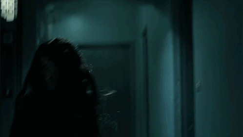 A Woman In A Leather Jacket Is Running Through A Dark Hallway In A Dark Room . GIF