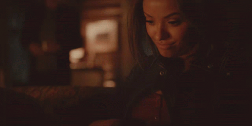 A Woman In A Leather Jacket Is Smiling And Looking At Something GIF