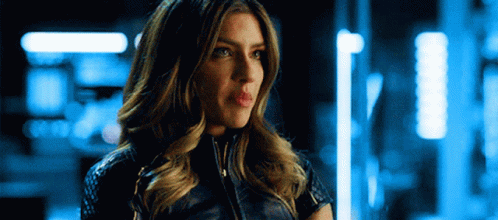 A Woman In A Leather Jacket Is Standing In A Dark Room . GIF