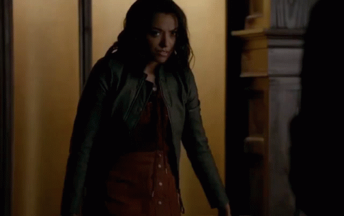 A Woman In A Leather Jacket Is Standing In Front Of A Door . GIF