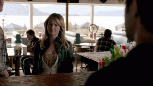 Woman In Leather Jacket Sitting At Bar Looking At Man GIF