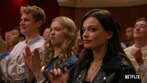 A Woman In A Leather Jacket Sits In A Crowd Of People Applauding GIF