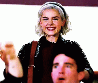 A Woman In A Leather Jacket Smiles While A Man Looks On GIF