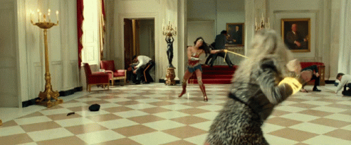 A Woman In A Leopard Print Dress Is Holding A Sword In A Room GIF