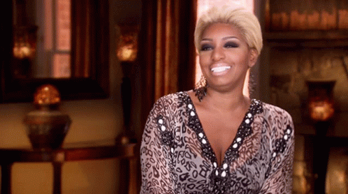 A Woman In A Leopard Print Dress Is Smiling In Front Of A Fireplace GIF