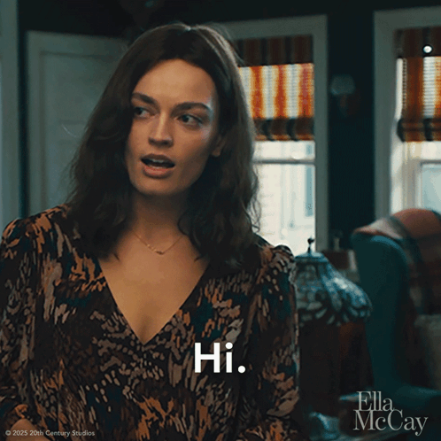 A Woman In A Leopard Print Dress Says Hi In Front Of A Window GIF