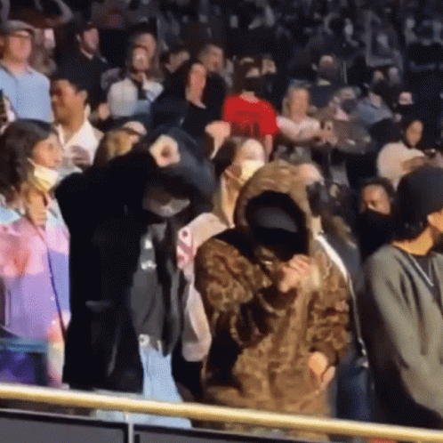 A Woman In A Leopard Print Hoodie Stands In A Crowd Of People Wearing Face Masks GIF