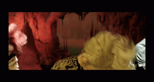 A Woman In A Leopard Print Shirt Is Dancing In Front Of A Red Wall GIF