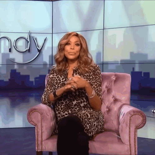 A Woman In A Leopard Print Shirt Sits In A Purple Chair In Front Of A Wall That Says Wendy GIF