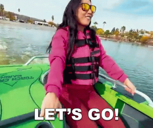 A Woman In A Life Jacket And Sunglasses Is Sitting In A Boat On A Lake And Says Let 'S Go . GIF