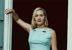 A Woman In A Light Blue Dress Is Standing In Front Of A Window . GIF