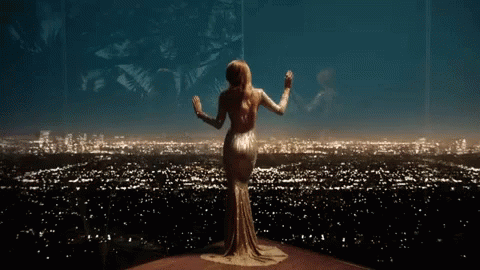 A Woman In A Long Dress Is Standing In Front Of A City Skyline At Night . GIF