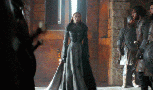 A Woman In A Long Gray Dress Is Standing In Front Of A Group Of Soldiers GIF