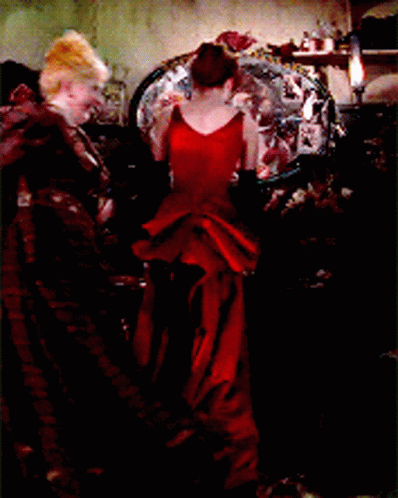 A Woman In A Long Red Dress Is Standing In Front Of A Mirror GIF