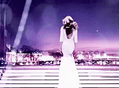 A Woman In A Long White Dress Is Standing On A Stage . GIF