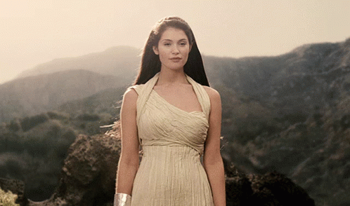 A Woman In A Long White Dress Stands In Front Of Mountains GIF