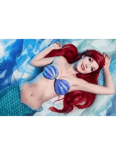 a woman in a mermaid costume is laying on a blue blanket