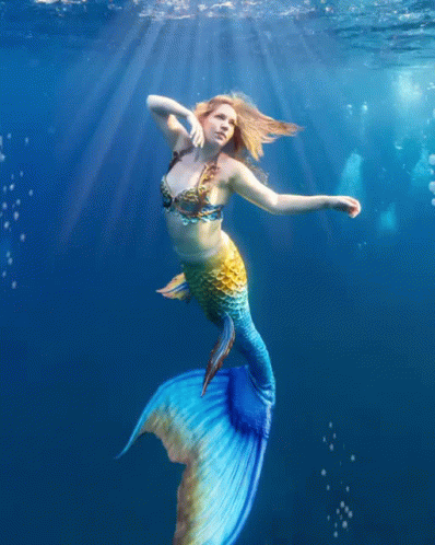 A Woman In A Mermaid Costume Is Swimming In The Water GIF