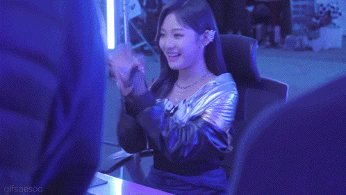 a woman in a metallic jacket is sitting in a chair in a dark room .