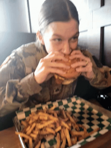 A Woman In A Military Uniform Is Eating A Sandwich And French Fries GIF