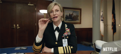A Woman In A Military Uniform Is Sitting At A Desk With A Netflix Logo In The Background GIF