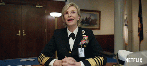 A Woman In A Military Uniform Sits At A Desk With A Netflix Logo In The Corner GIF