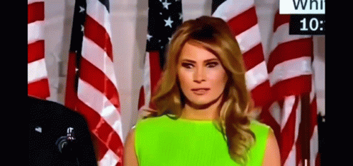 A Woman In A Neon Green Dress Is Standing In Front Of A Wall Of American Flags . GIF